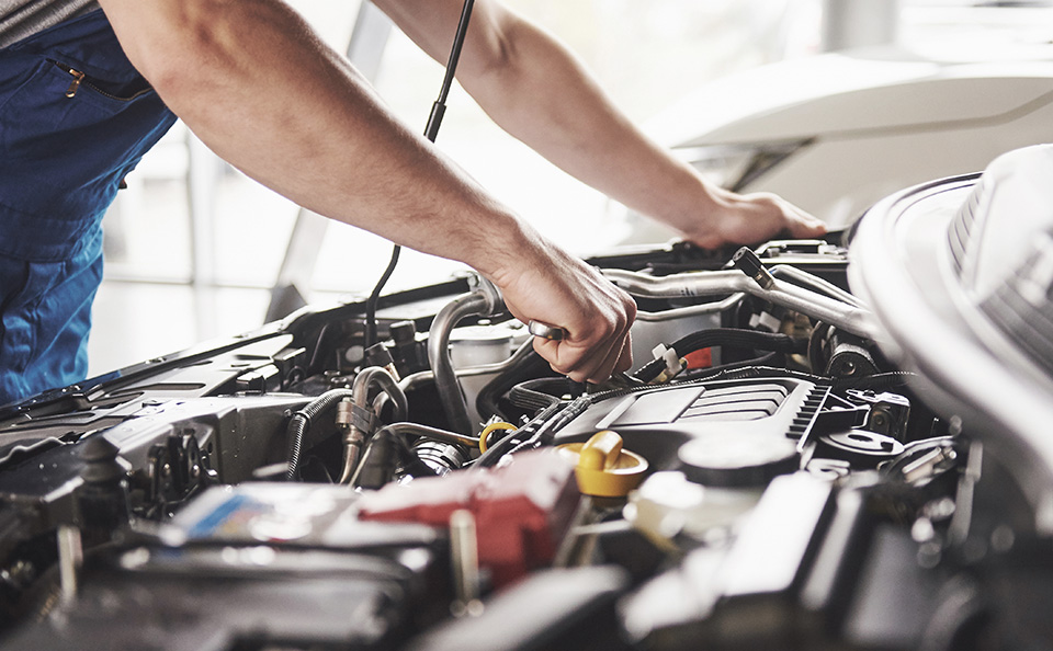 Close-up of a mechanic in blue overalls using a wrench to work on a car engine.